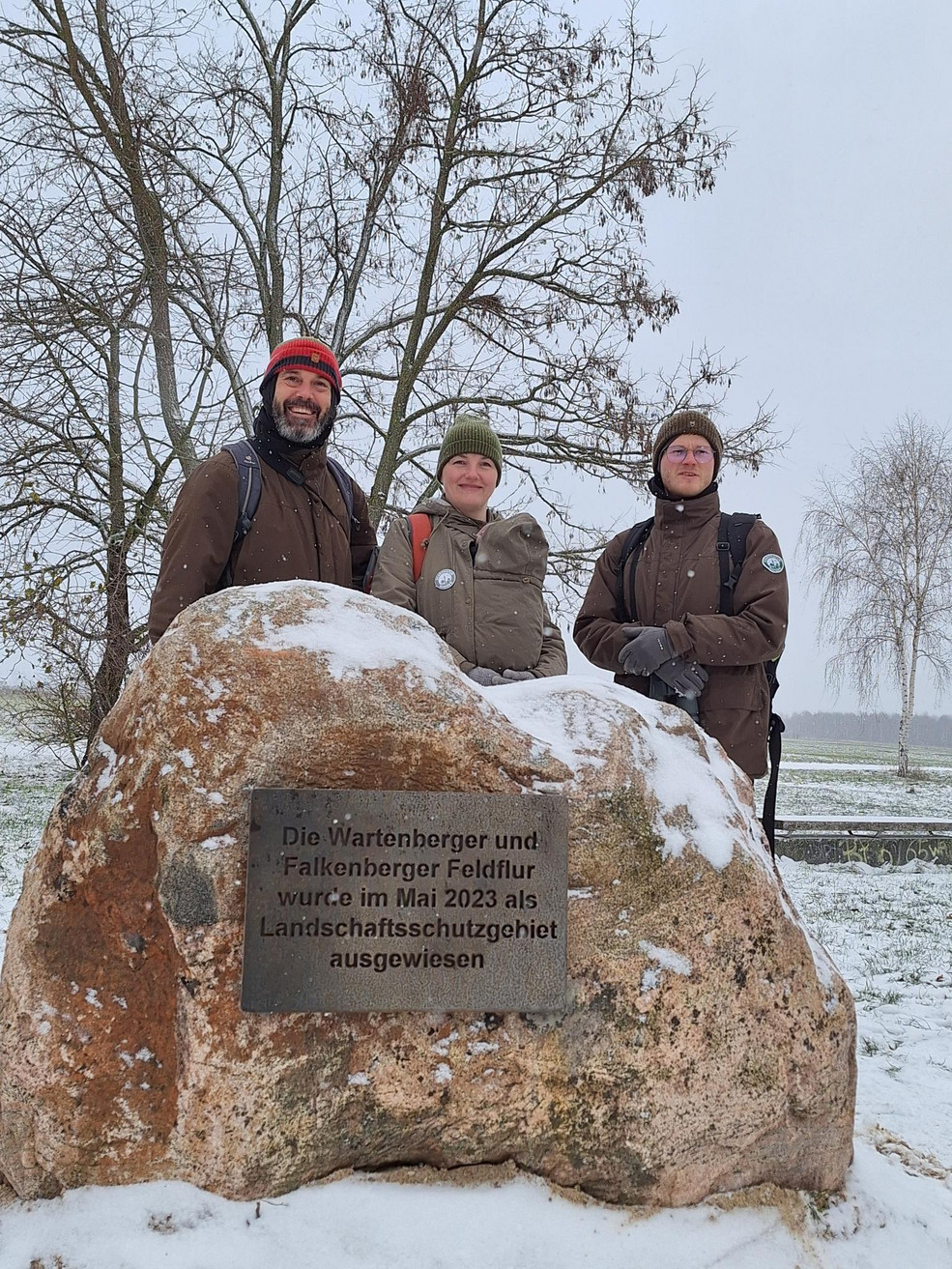 Die Stadtnatur-Ranger*innen Frank Schneider, Mira Langrock und Lutz Kröner stehen hinter dem Findling und schauen in die Kamera.