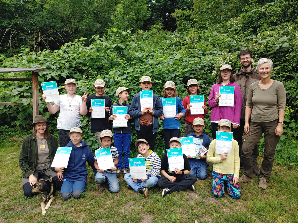 Gemeinsam mit drei Stadtnatur-Ranger*innen blicken die Junior-Ranger*innen in die Kamera und halten jeweils eine Urkunde in der Hand.