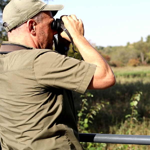 Ein Mann im T-Shirt schaut durch mit seinem Fernglas auf die natürliche Landschaft. 